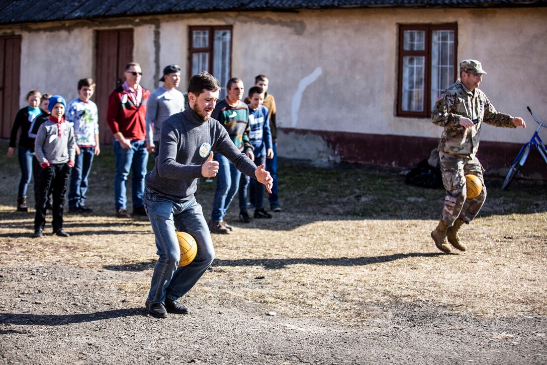 A soldier and a man race each other while each holds a ball in between their legs.