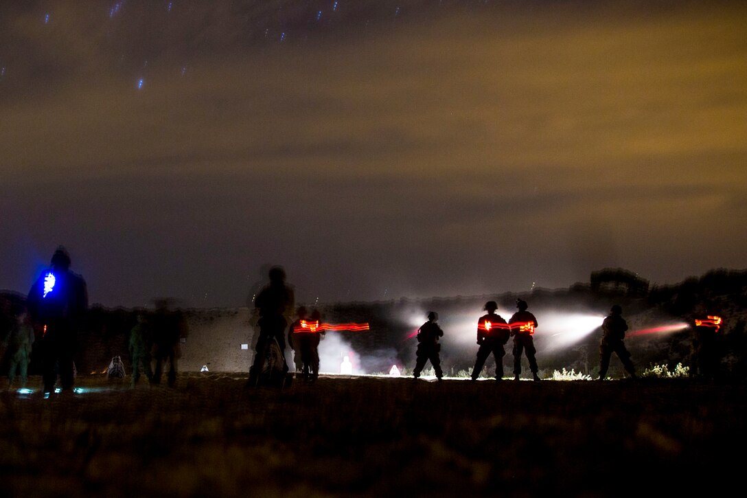 Marines, shown as silhouettes, conduct training in a field at night, giving off red beams of light.
