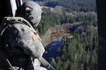 A crew chief on a Black Hawk helicopter watches the placement of a water bucket pendent and relays its information to the pilots during a check ride with the U.S. Forest Service. Washington National Guard aviators conduct water bucket training annually in preparation for wildland fire response.