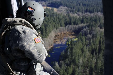 A crew chief on a Black Hawk helicopter watches the placement of a water bucket pendent and relays its information to the pilots during a check ride with the U.S. Forest Service. Washington National Guard aviators conduct water bucket training annually in preparation for wildland fire response.