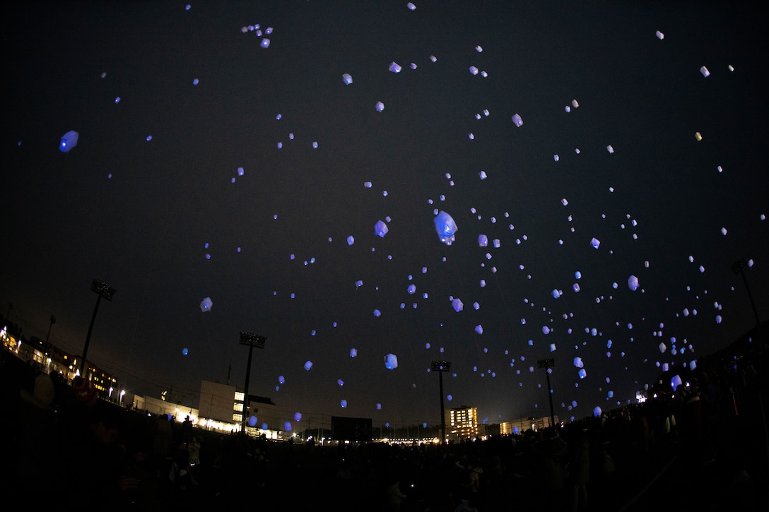 Purple colored paper lanterns float upward in a dark sky.