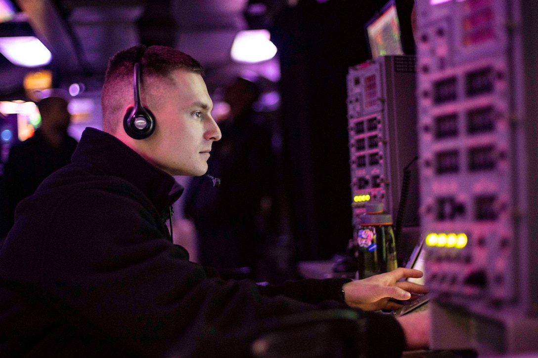 A service member stands watch at a console aboard a ship.