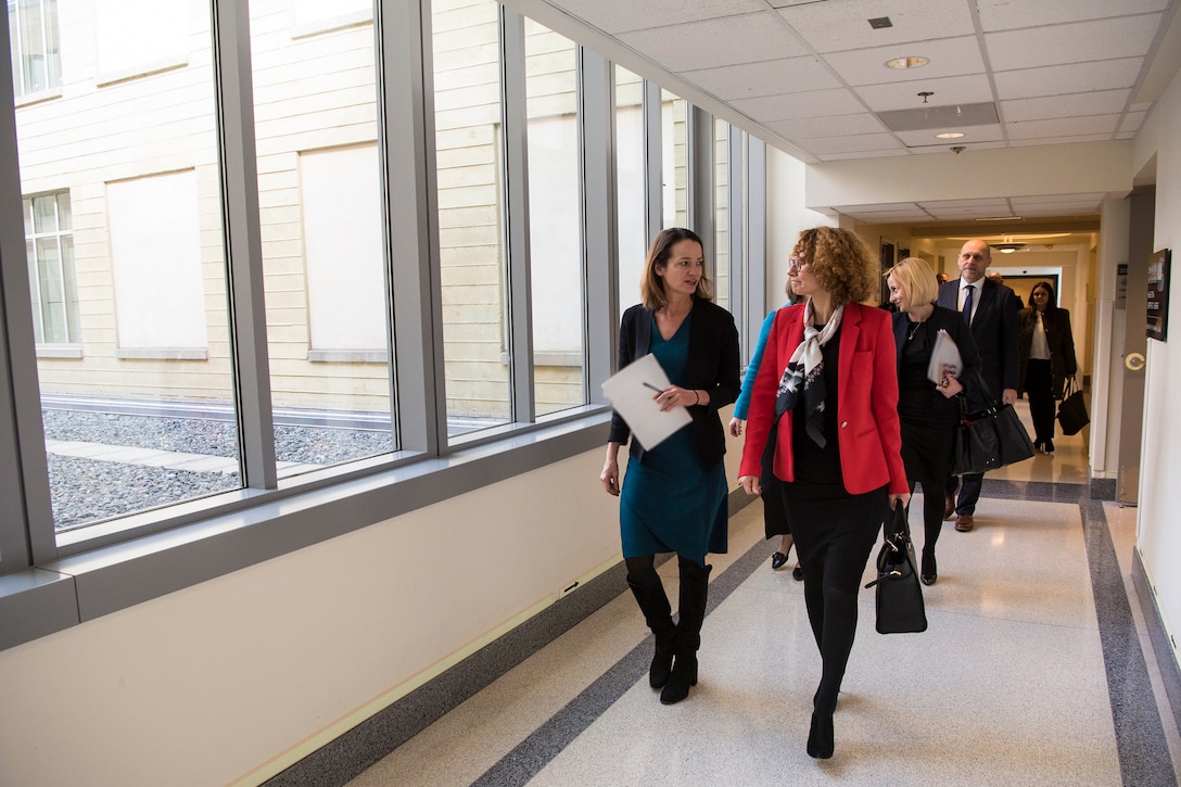 Two women walk down a hallway with a group of people behind them.