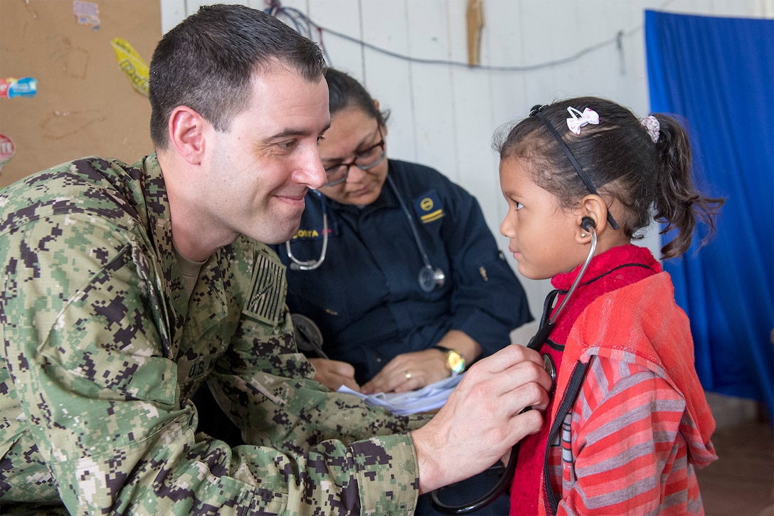 A service member helps a young patient listen to her heartbeat.