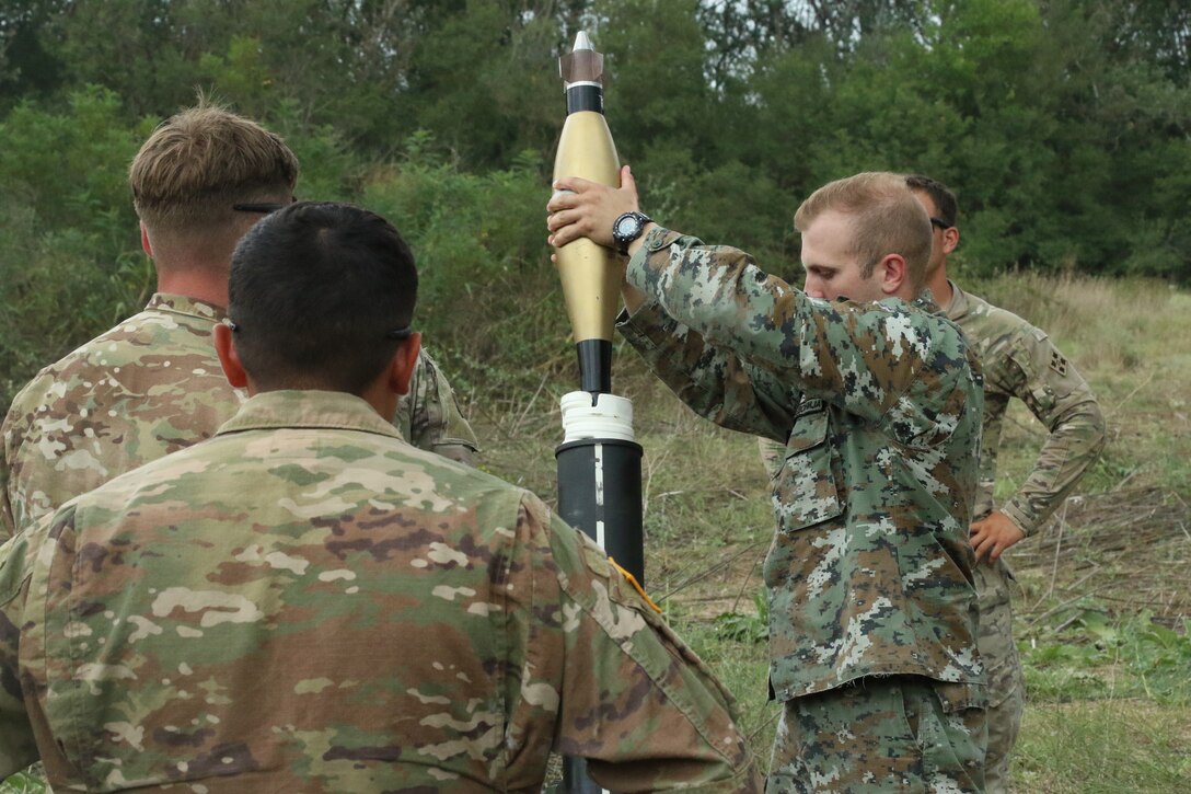 American soldiers observe a North Macedonian soldier placing mortar in mortar tube during an exercise.