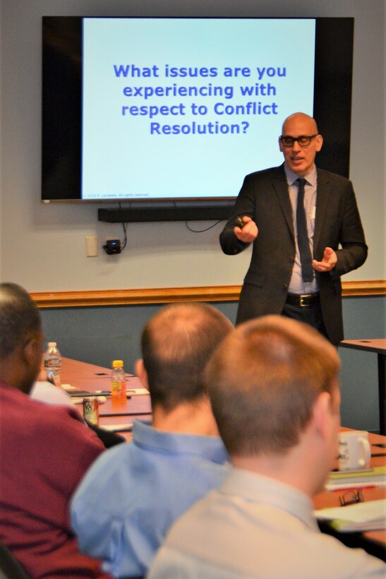 Man in suit speaks to class with a conflict resolution slide in the background