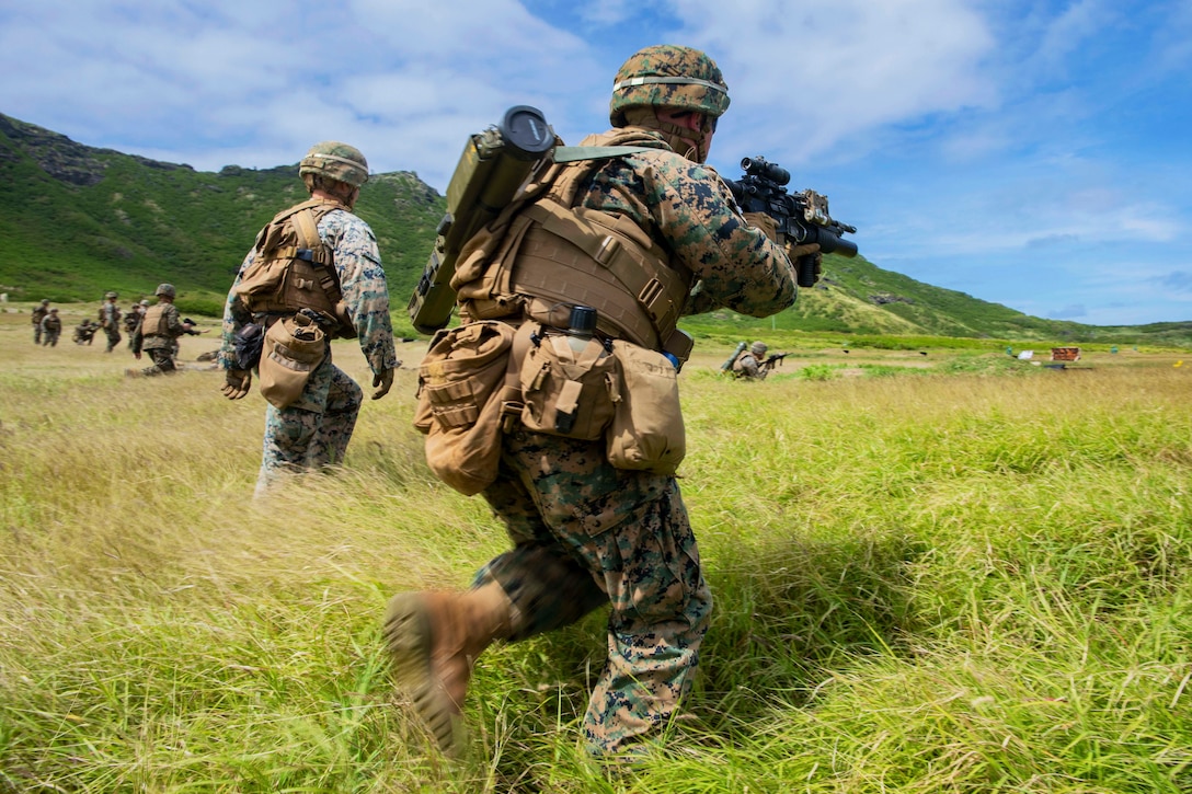 Marines race through a field with weapons drawn.