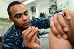 Hospital Corpsman 3rd Class Fernando Javier administers a typhoid shot to a patient in a medical room aboard the Nimitz-class aircraft carrier USS Harry S. Truman (CVN 75).