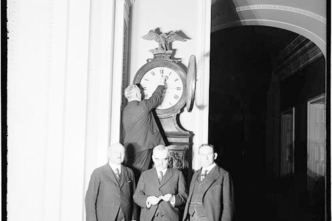 Three men stand in front of a large clock in 1918 while a fourth man changes the hands on the clock.