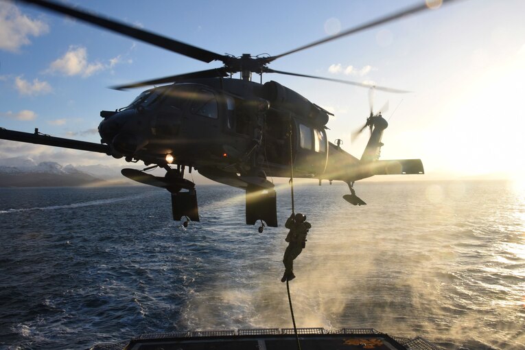 A coast guardsman lowes onto a cutter from a helicopter.
