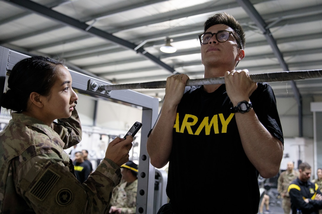 A soldier keeps time while another does chin ups.