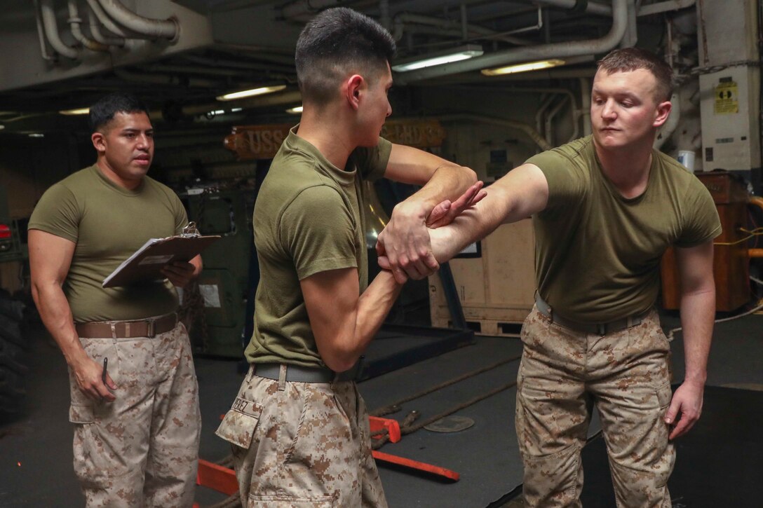 U.S. Marine Cpl. Emilio Perez, a satellite operator with the 22nd Marine Expeditionary Unit, executes a cross body grip control tecnique on Cpl. David Lynam, a motor transport mechanic also with the 22nd MEU, as Marine Corps Martial Arts Program instructor Sgt. Michael Romero looks on in the well deck of the Wasp-class amphibious assault ship USS Kearsarge. Sgt. Romero, a satellite operator with Combat Logistics Battalion 22, evaluated the Marines on their understanding and performance of gray and green belt MCMAP  techniques. Marines and Sailors with the 22nd MEU and Kearsarge Amphibious Ready Group are deployed to the 5th Fleet area of operations in support of naval operations to ensure maritime stability and security in the Central Region, connecting the Mediterranean and the Pacific through the western Indian Ocean and three strategic choke points. (U.S. Marine Corps photo by Lance Cpl. Tawanya Norwood)