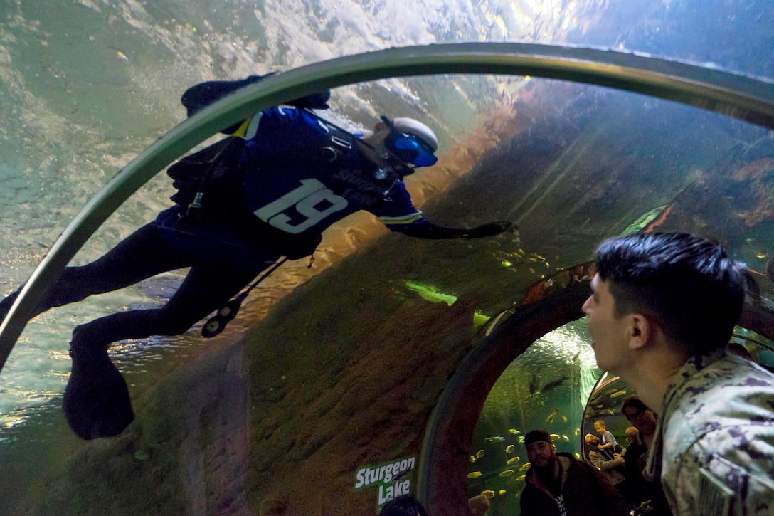 A diver looks out at visitors from inside a glass aquarium.