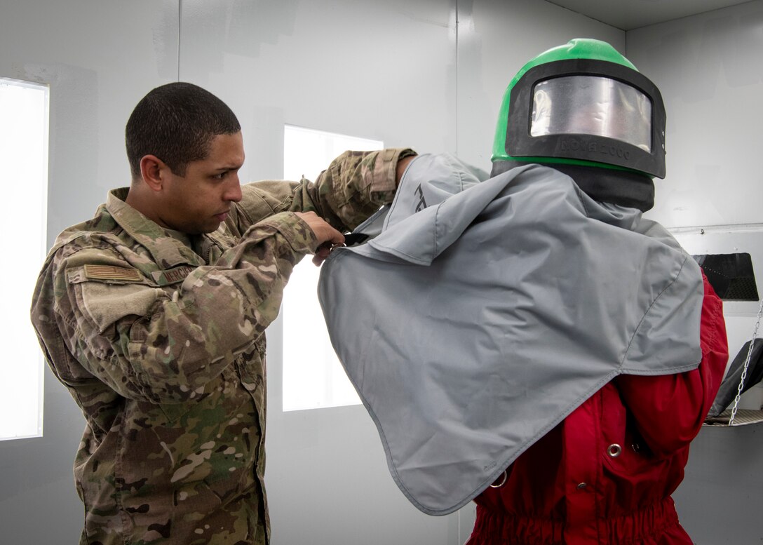 U.S. Air Force Tech. Sgt. Jonathan, 33rd Maintenance Squadron Low Observable Corrosion Control Section noncommissioned officer in charge, helps Airman 1st Class Evan Green, 33rd MXS LO aircraft structural maintenance journeyman, dawn a protective helmet Feb. 21, 2019, at Eglin Air Force Base, Fla. Together, Mercier and Green have worked hard at making the Corrosion Compound to be a fully functional operation. (U.S. Air Force photo by Airman 1st Class Daniella Peña-Pavao)