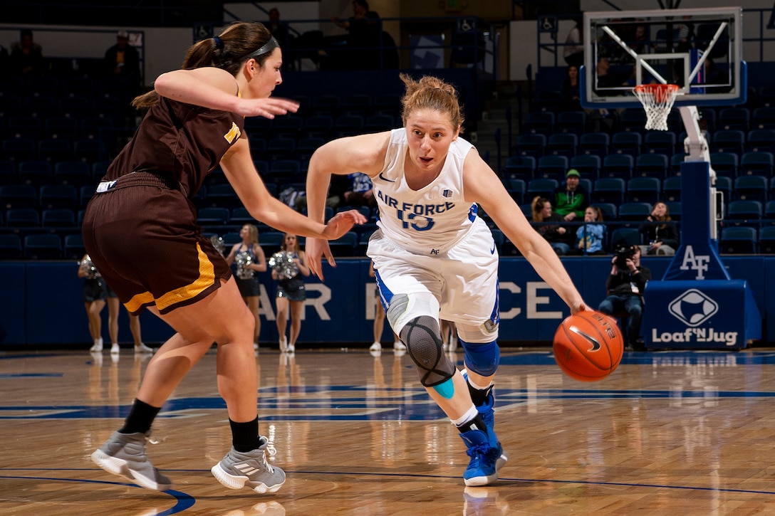 A woman basketball player dribbles the ball as she runs by another player.