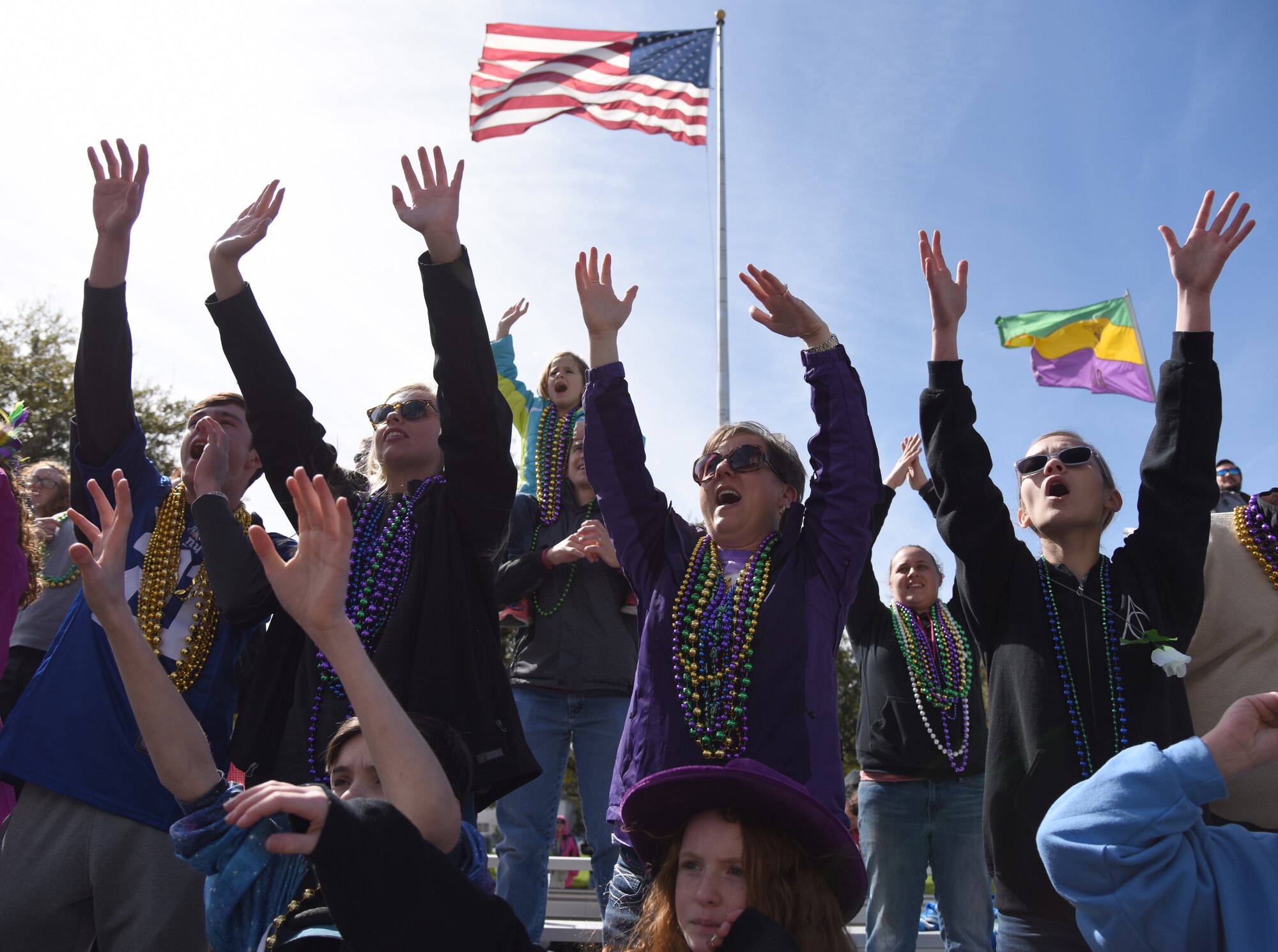 Keesler personnel and their families raise their hands and yell for "throws" from parade floats during the Gulf Coast Carnival Association Mardi Gras parade in Biloxi, Mississippi, March 5, 2019. Keesler personnel participate in local parades every Mardi Gras season to show their support of the communities surrounding the installation. (U.S. Air Force photo by Kemberly Groue)
