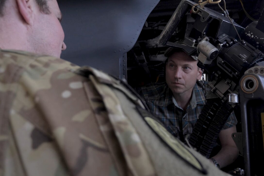 A man listens to a soldier explaining a helicopter door gun.