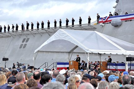 Cmdr. Christopher K. Brusca, the commanding officer of the Navy's newest littoral combat ship, USS Charleston (LCS 18), delivers his remarks while his crew watch on from the ship during the commissioning ceremony.