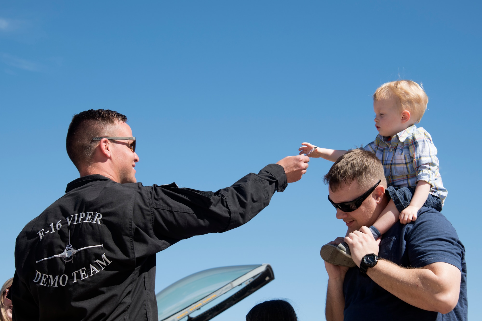 U.S. Air Force Staff Sgt. Trevor Griswold, F-16 Viper Demonstration Team electrical and environmental systems craftsman, hand a sticker to a child on the flight line at Davis-Monthan Air Force Base, Ariz., March 3, 2019.