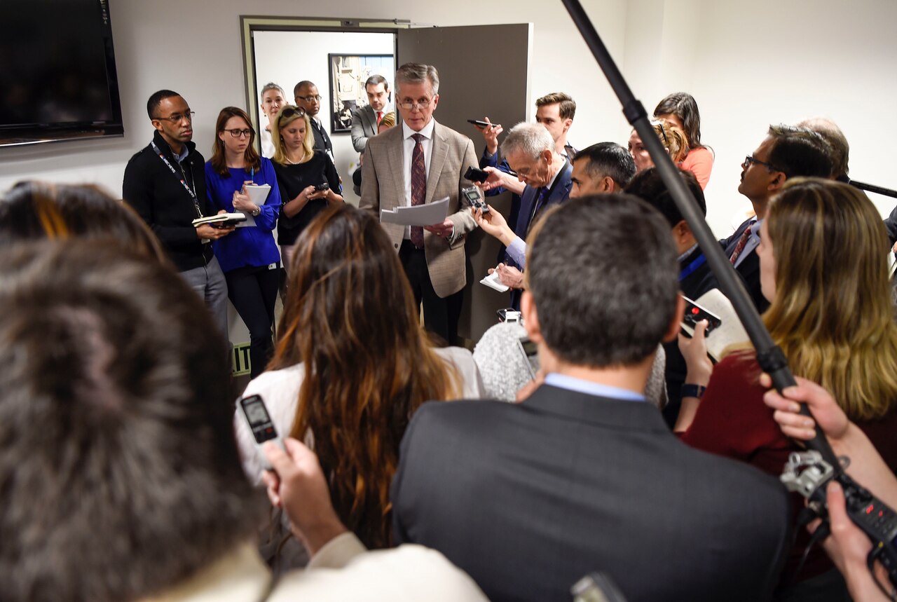 A man is surrounded by reporters as he speaks.