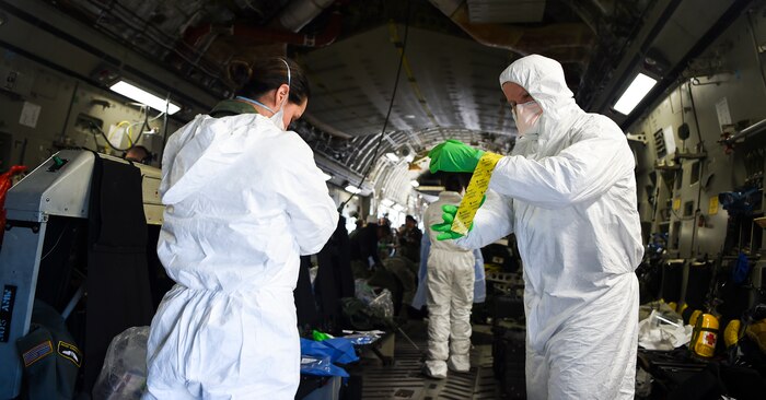 Airmen assist one another in donning their personal protective equipment March 6, 2019, while on-board an Air Force C-17 Globemaster III during transportation isolation system training at Joint Base Charleston, S.C. Engineered and implemented after the Ebola virus outbreak in 2014, the TIS is an enclosure the Department of Defense can use to safely transport patients with highly contagious diseases.