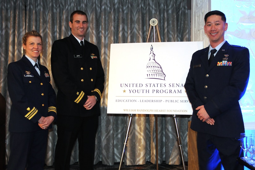 Three military officers stand in front of sign.