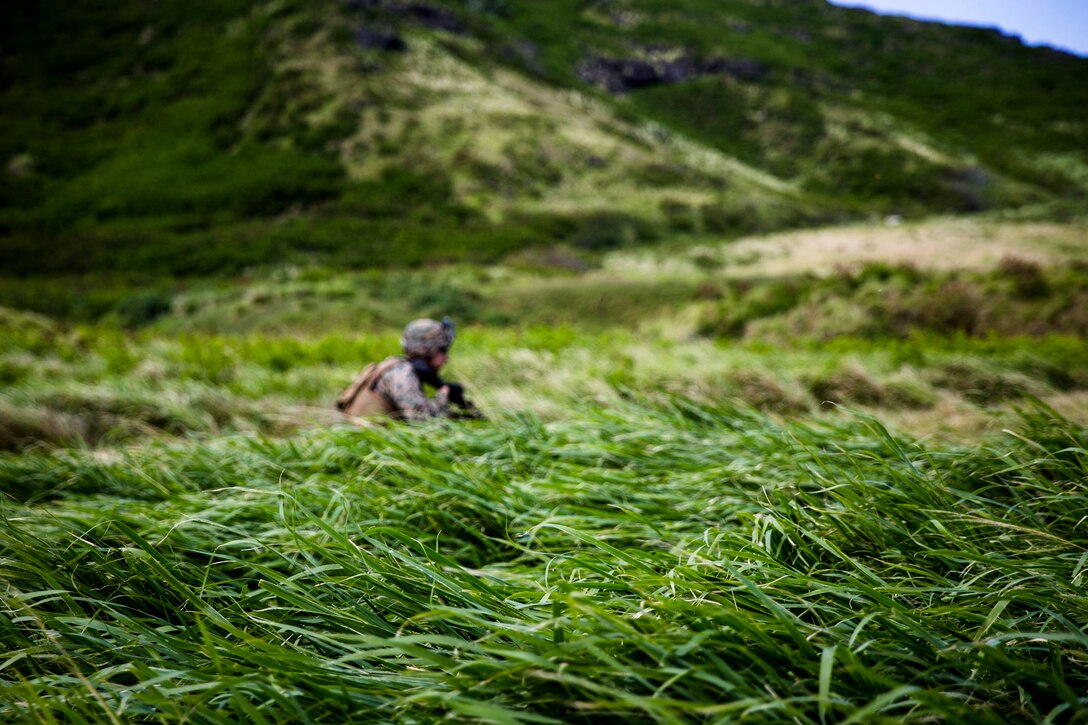 A Marine walks behind through a large grassy field.