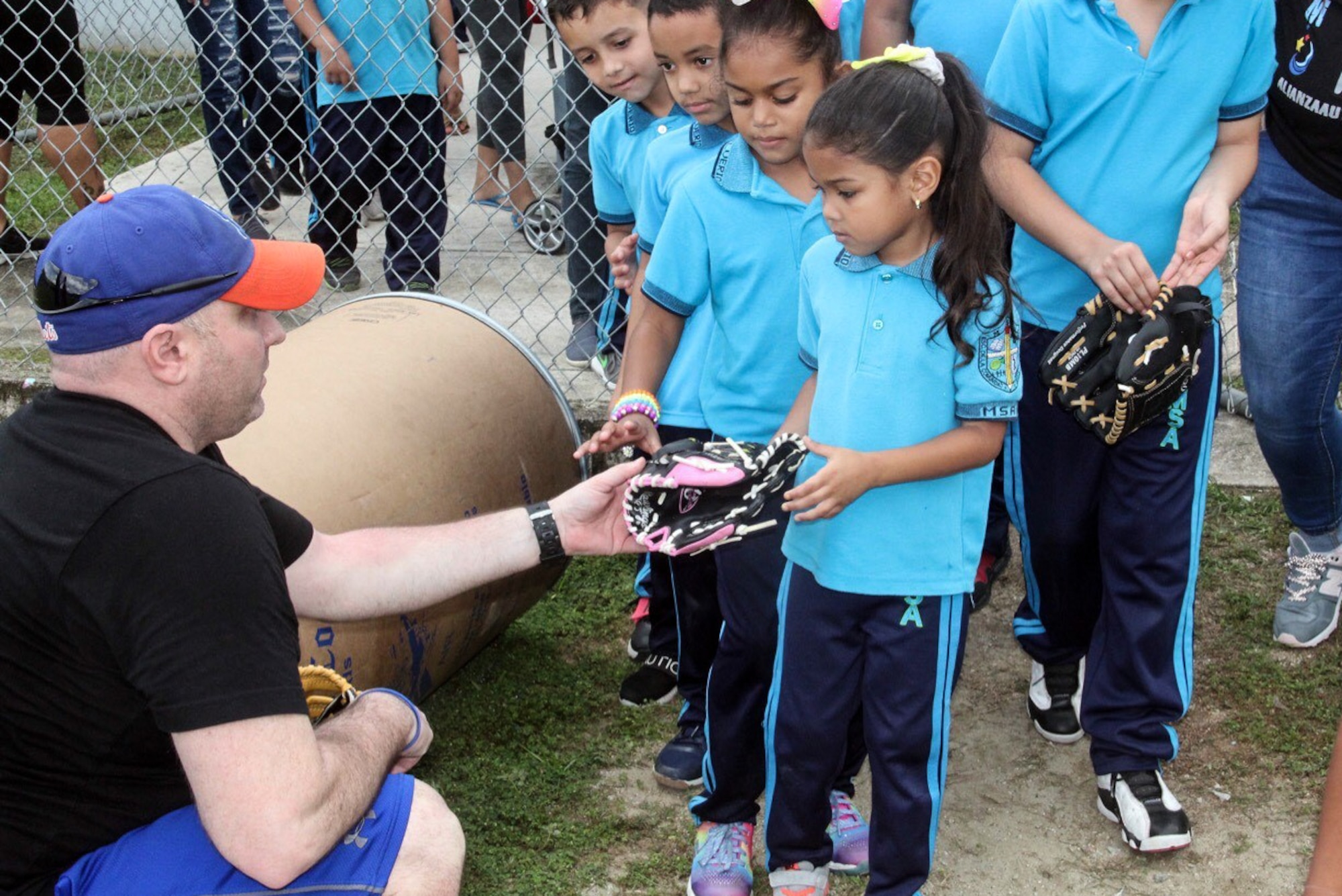 Air Force Chief Master Sgt. Greg Souders, left, the superintendent of the 193rd Special Operations Logistics Readiness Squadron, Pennsylvania Air National Guard, passes out baseball gloves to children during a Baseball Miracles event.