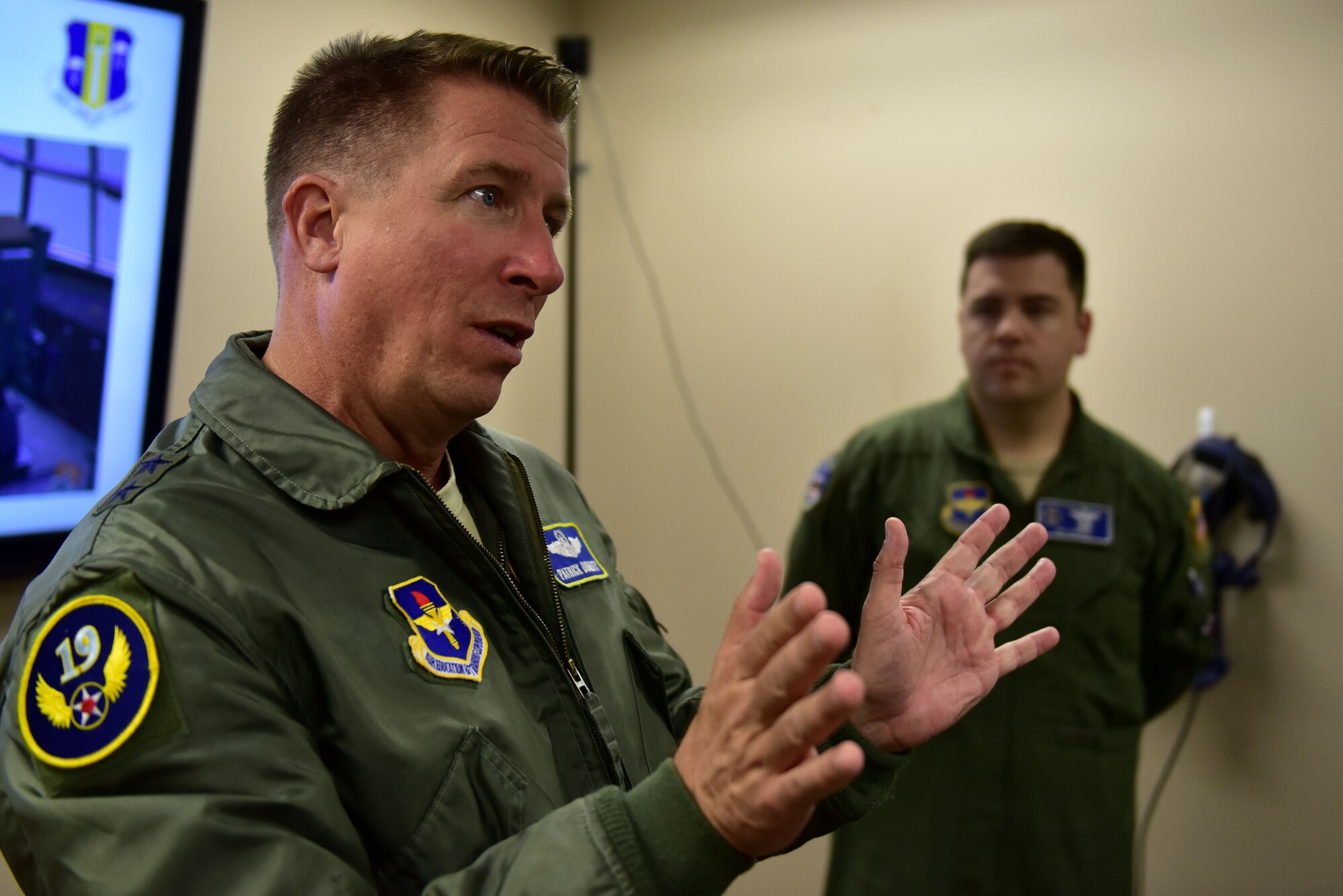 A man wearing the Air Force flight suit talks to an audience.