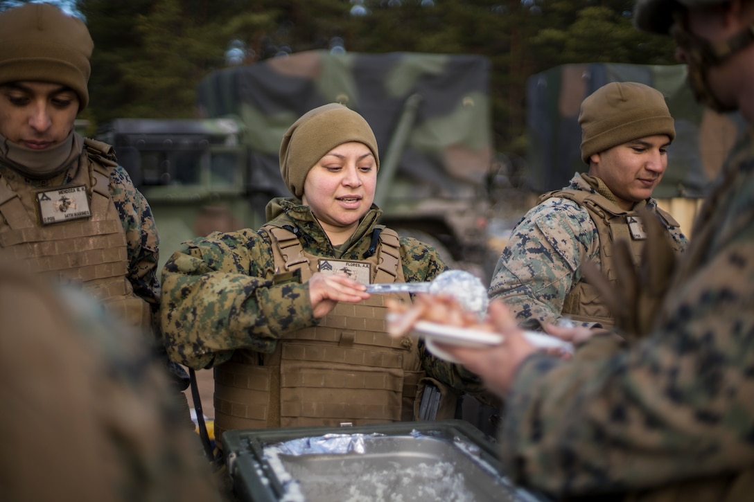 A Marine standing between to others  serves food on a plate.