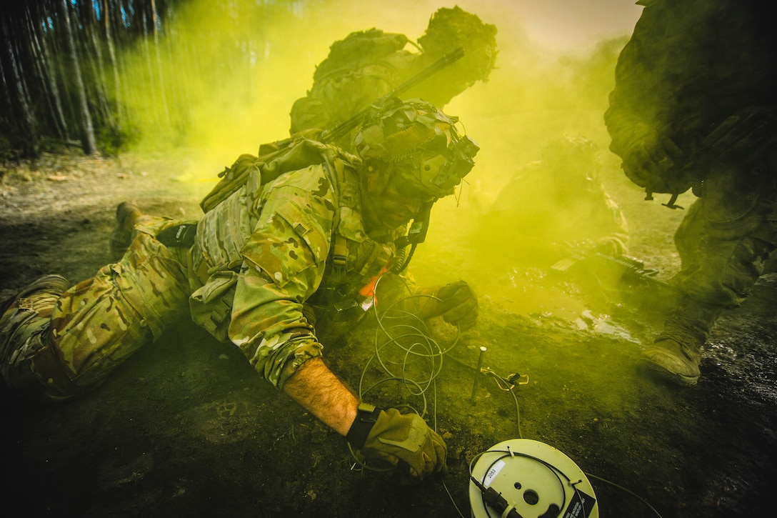 A soldier lies on the ground surrounded by green smoke.