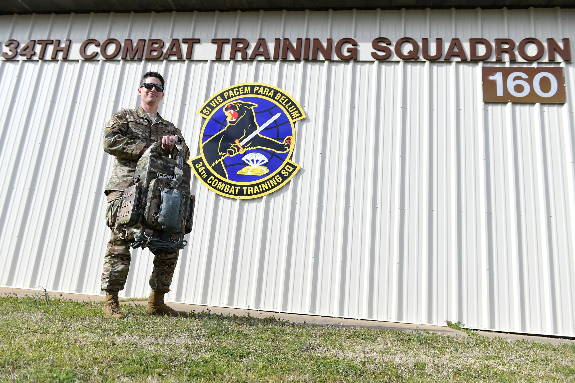 A man holds a backpack in front of a building.