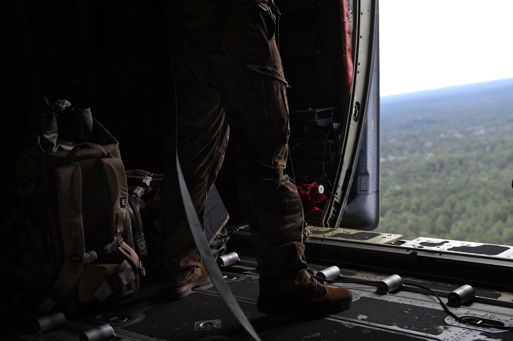 Feet and lower legs are shown beside a backpack and an open door on a C-130J.