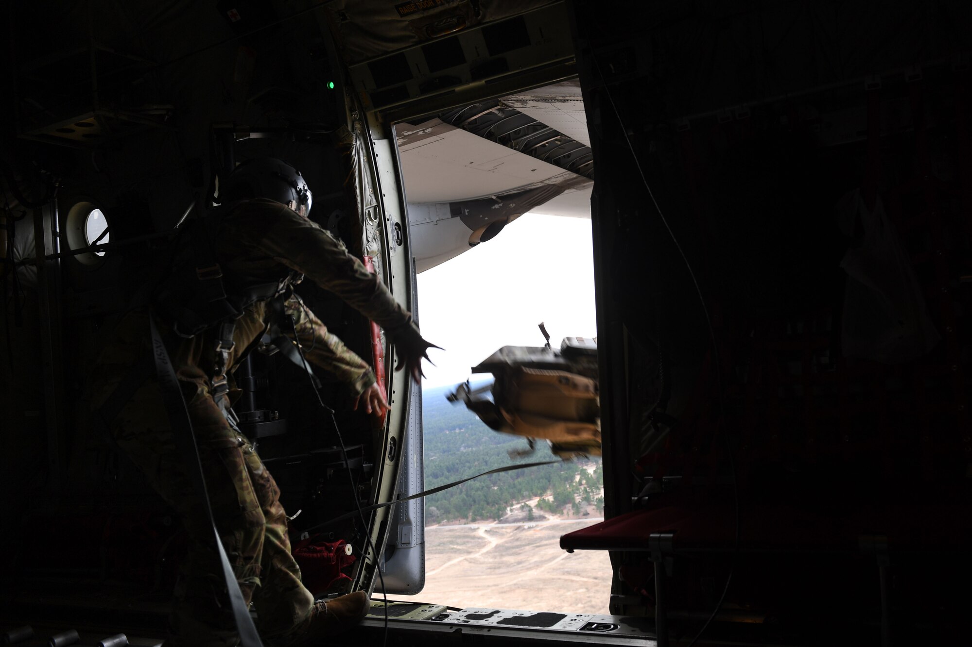 An Airman throws a backpack out of a C-130J, while in the air.