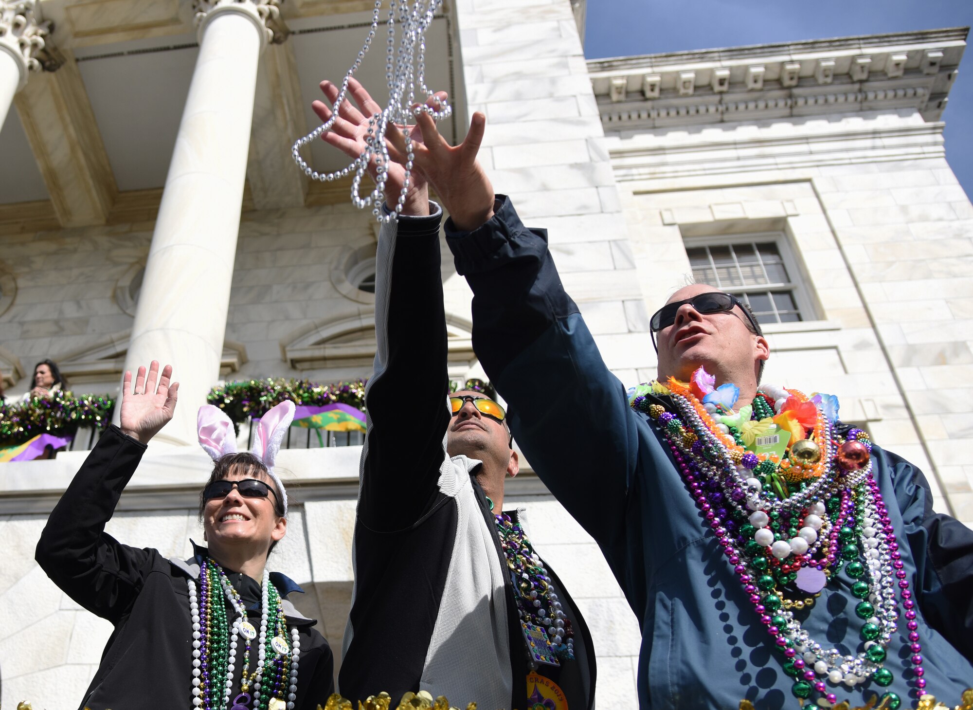 U.S. Air Force Col. Debra Lovette, 81st Training Wing commander, raises her arm for "throws" as Chief Master Sgt. Ricardo Russo, Keesler Medical Center superintendent, and Col. Todd Weyerstrass, Second Air Force vice commander, reach for strands of beads tossed to them from floats during the Gulf Coast Carnival Association Mardi Gras parade in Biloxi, Mississippi, March 5, 2019. Keesler personnel participate in local parades every Mardi Gras season to show their support of the communities surrounding the installation. (U.S. Air Force photo by Kemberly Groue)