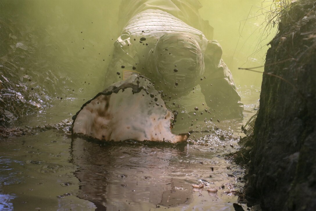 A service member crawls through mud.