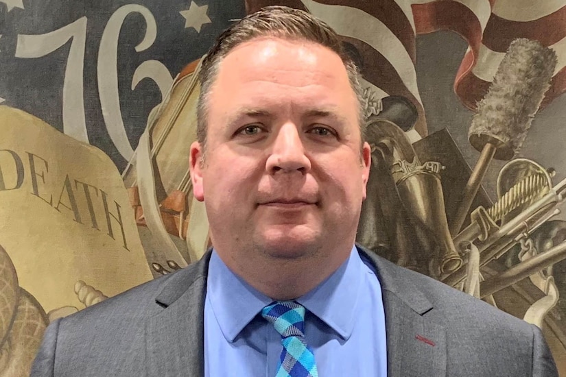 A man poses for an official photo in a suit.