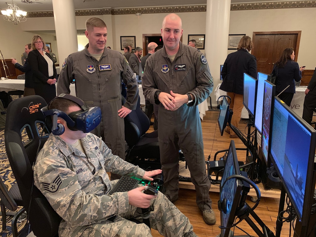 Lt. Col. Joe Stallings (left), 12th Flying Training Wing Innovation Director, and Capt. Calogero San Filippo (right), Pilot Training Next instructor pilot, discuss virtual-reality flying technology while Staff Sgt. Joseph Sabin, Air Education and Training Command, flies a VR sortie at the PTN Technology Expo at Joint Base San Antonio-Randolph, Texas, March 12, 2019.  Flying training wings will formally begin integrating innovations from PTN into the undergraduate pilot training curriculum beginning May 31, 2019.