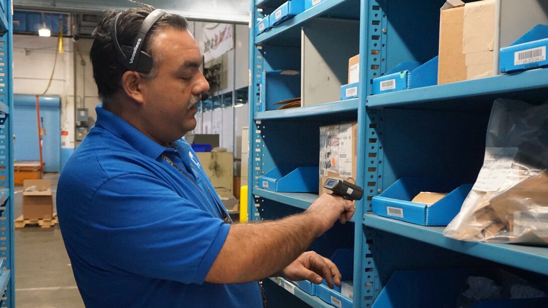 Anthony Kotta selects items from a warehouse shelf using voice pick technology