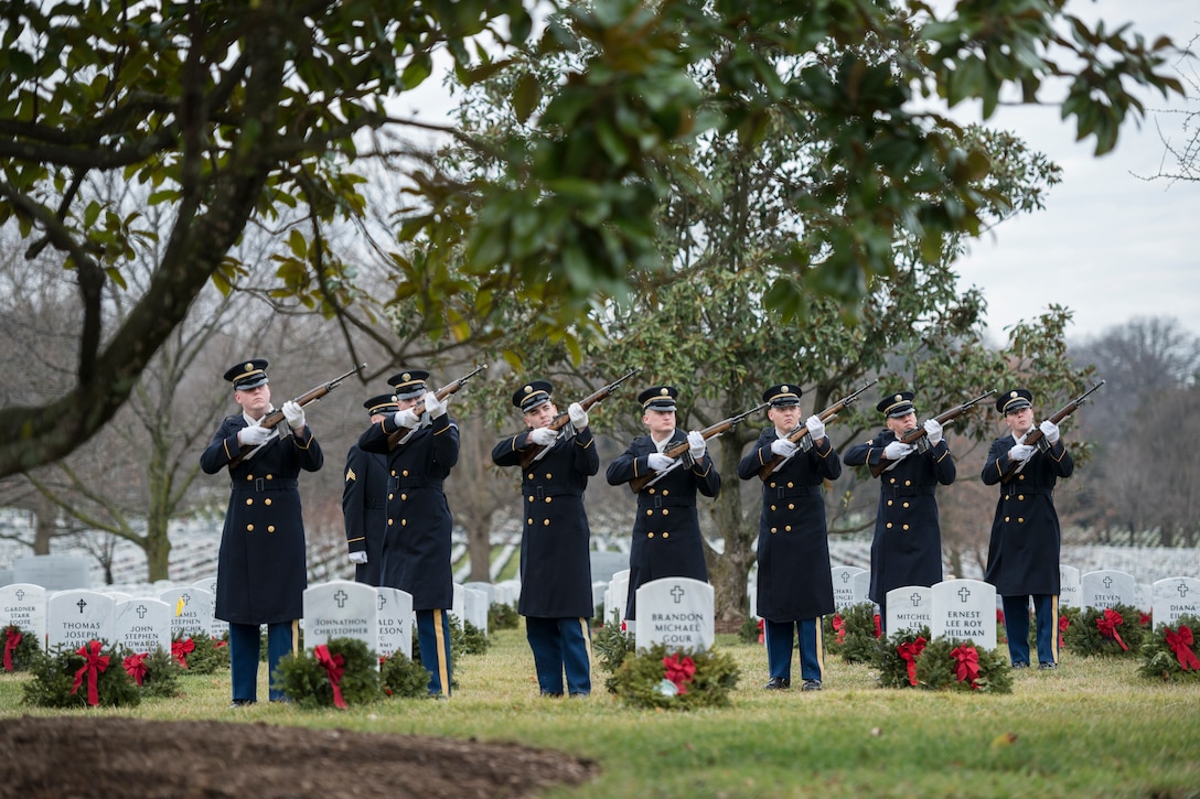 Soldiers fire rifles in a cemetery.