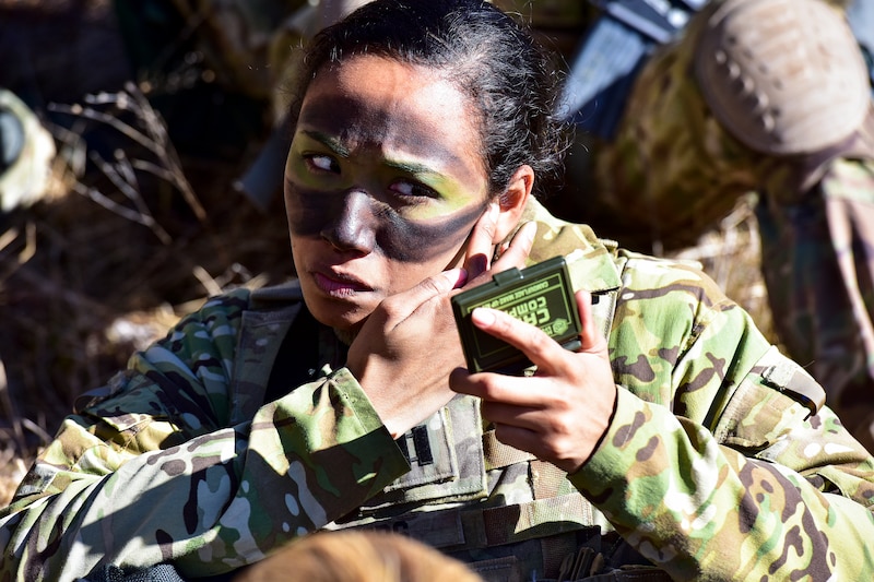 A soldier paints her face green and black while holding a small mirror.