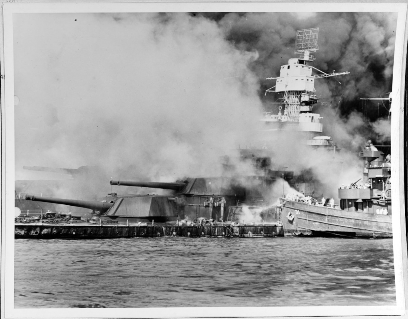 USS Tern (AM-31) fighting fires aboard the sunken USS West Virginia (BB-48), Dec. 7, 1941, immediately after the Japanese raid. Note radar antenna, paravanes and 16/45 twin gun turrets on the battleship. (Official U.S. Navy Photograph, from the collections of the Naval History and Heritage Command)