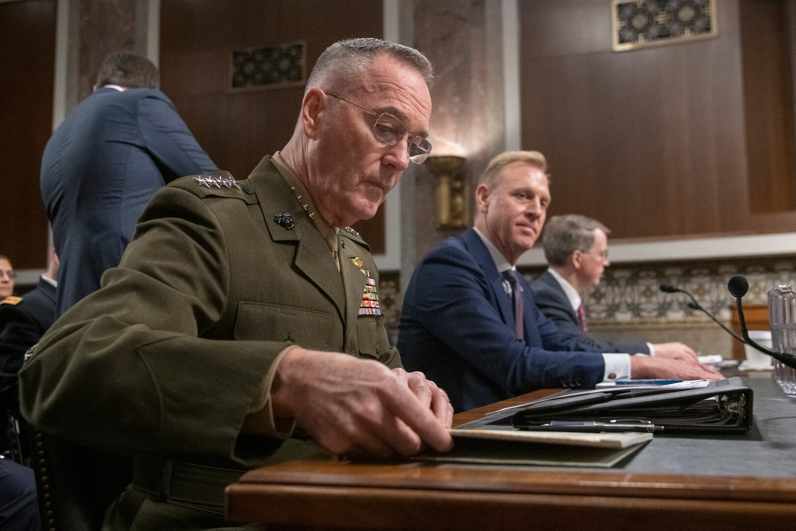 Three men sit at a desk, one in military uniform.