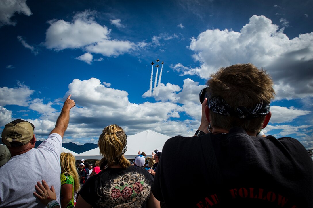 A crowd points toward the sky, where four F-16 Fighting Falcons are flying in a diamond formation.