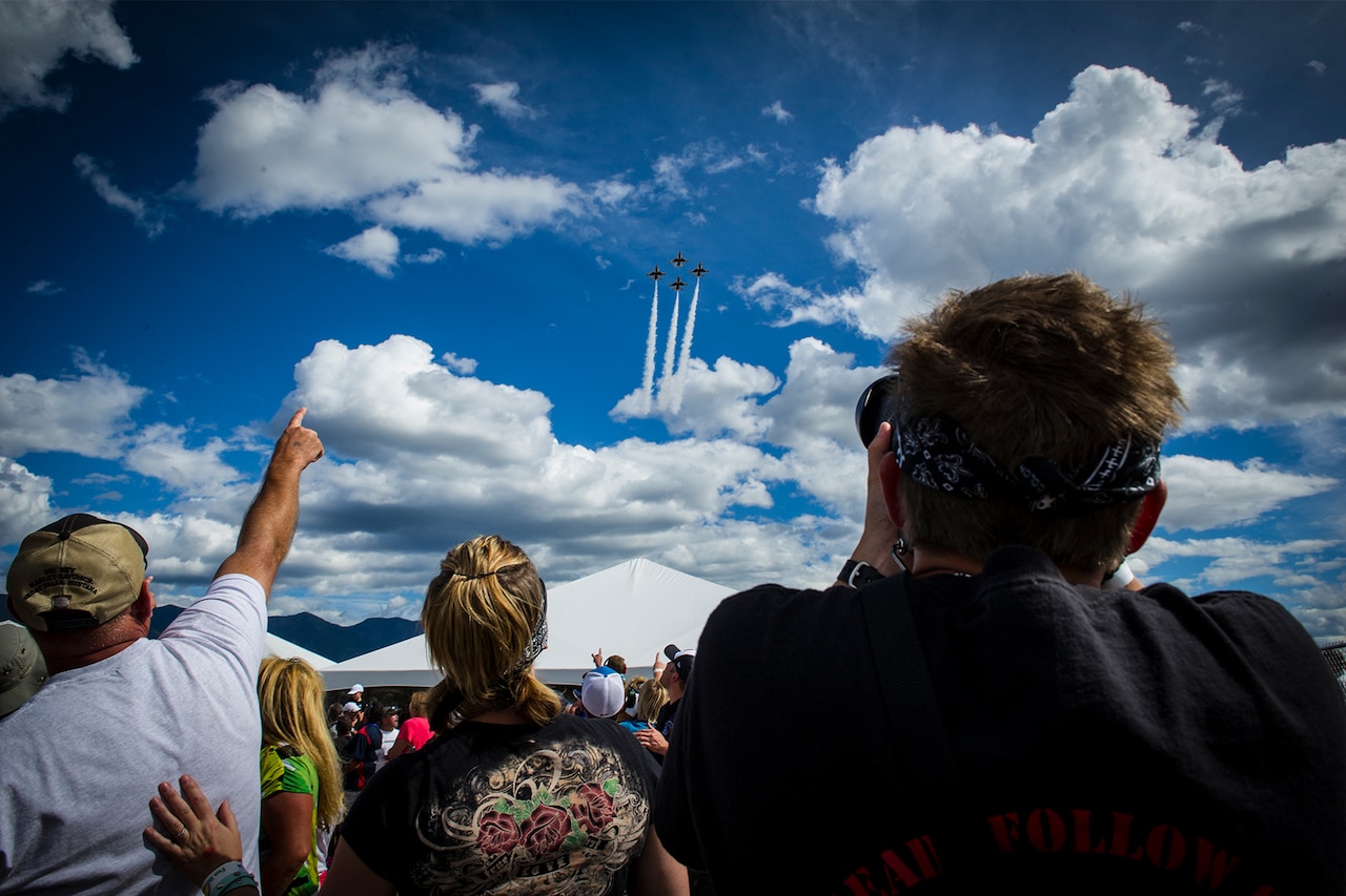 A crowd points toward the sky, where four F-16 Fighting Falcons are flying in a diamond formation.