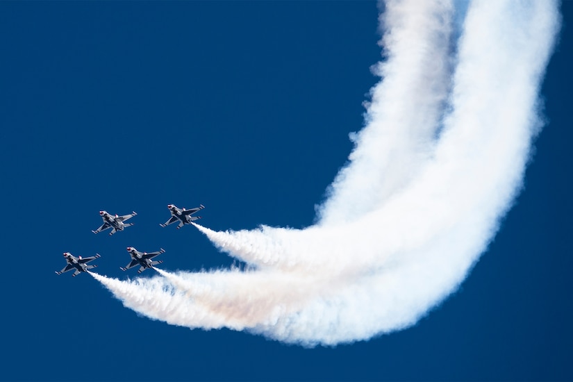 Four F-16 Fighting Falcons emit heavy condensation trails in a clear blue sky.