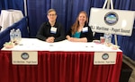 Two female associates sitting behind a booth.