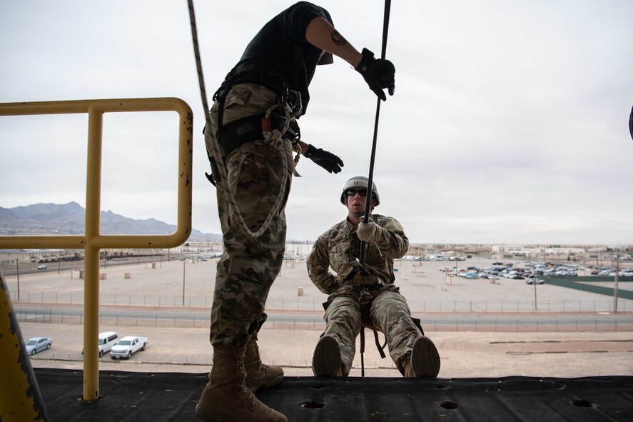 An instructor teaches a trainee on proper rappelling techniques