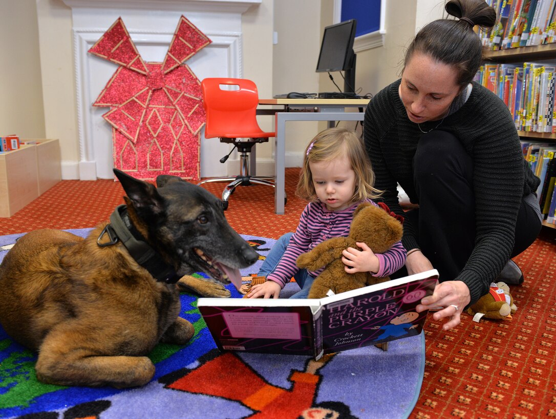 Retired Military Working Dog Vvonya enjoys a story with Ava Mort, 1, and Kimberly Mort, wife of Master Sgt. Joshua Mort, Team Mildenhall member, at the story and craft event at the base library on RAF Mildenhall, England, March 13, 2019. Children had the opportunity to make crafts, pet Vvonya and watch a military working dog demonstration at the event celebrating K9 Veterans’ Day. (U.S. Air Force photo by Karen Abeyasekere)