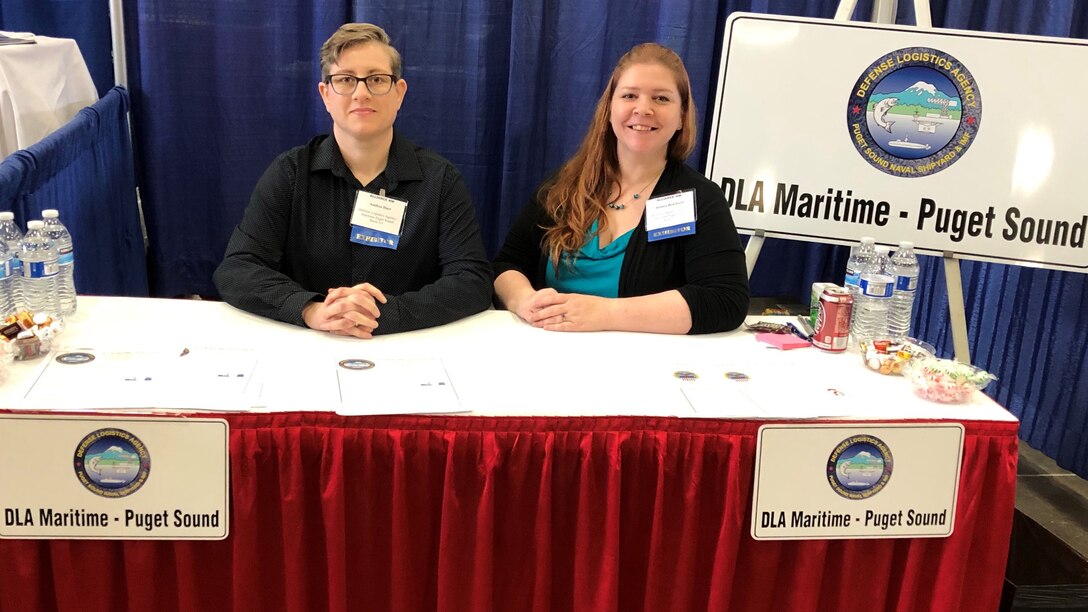 Two female associates sitting behind a booth.